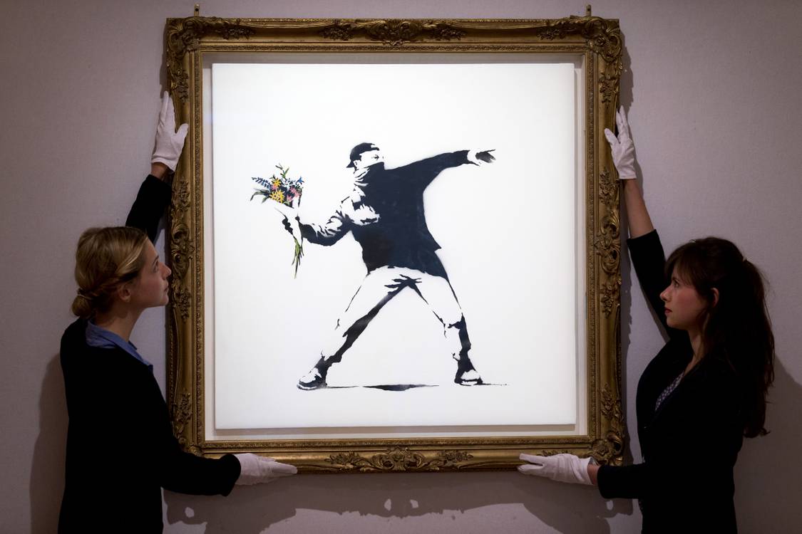 Gallery handlers in white gloves hanging a framed Banksy Flower Thrower